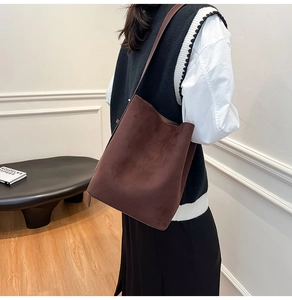 Detail of a large dark brown suede tote bag worn over the shoulder by a model