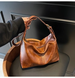 Gros plan sur la texture du cuir marron et le logo métallique du sac hobo
