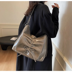 Taupe patent leather tote with pleated bow detail shown on shoulder for size and drape