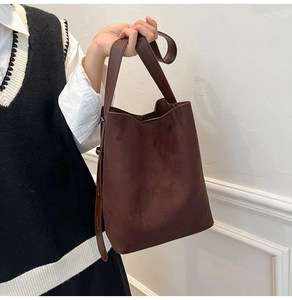 Detailed close-up of dark brown suede bucket bag with leather strap and metal buckle