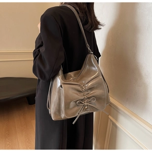 Detail of greyish-brown tote with bow accent, pleated front pocket and contrast stitching