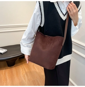 Detail view of large dark brown suede bucket bag worn over the shoulder in a minimalist room