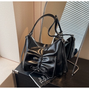 Detail of black glossy shoulder bag featuring a large bow pocket and white contrast stitching