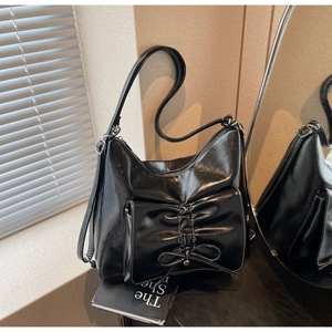 Close-up of black glossy shoulder bag with white contrast stitching and bow detail