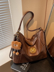 Vintage brown leather tote bag with gold M logo and plush doll pendant on table