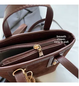 Détail d'une fermeture éclair dorée sur un sac en daim marron avec pendentif cœur et pompon