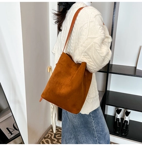 Close-up of brown suede bucket bag with leather strap worn over a white sweater