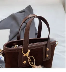 Détail du sac seau marron foncé montrant la texture suède et les rivets dorés