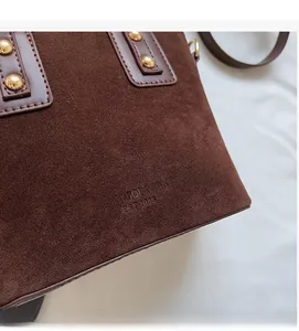 Détail du sac seau en daim marron avec logo embossé et finitions en rivets dorés