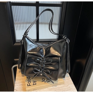 Detail of glossy black leather tote bag featuring a decorative bow-shaped front pocket