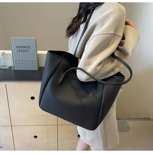 Side view of black lychee grain leather tote bag worn by a model in a minimalist room