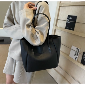 Close-up of black lychee grain texture and minimalist text detail on the leather tote bag