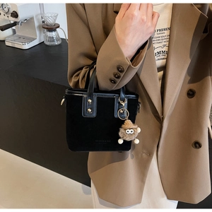 Détail d'un mini cabas noir en daim avec un charmant pendentif monstre en peluche