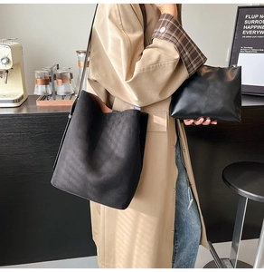 Detail of minimalist black suede bucket bag and leather pouch shown in a cafe setting