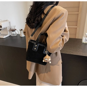 Détail d'un sac seau en daim noir avec pendentif peluche sur un mannequin chic
