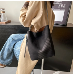 Detail shot of a black suede bucket bag with a brown lining and adjustable leather strap