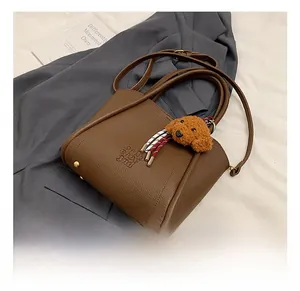 Detail of dark brown leather bucket bag featuring embossed text and plush poodle pendant