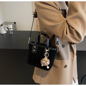 Gros plan du sac seau noir en daim avec un pendentif décoratif monstre en peluche marron