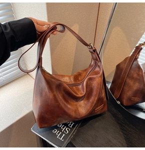 Détail d'un sac hobo vintage marron foncé avec logo métallique et forme de croissant chic