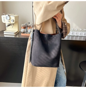 Detail of a large black suede bucket bag worn on shoulder in a luxury cafe setting