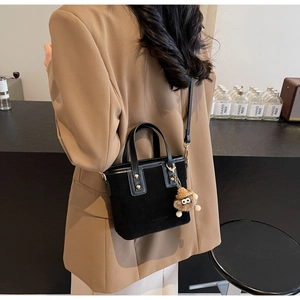Détail d'un sac cabas noir mat avec un pendentif monstre en peluche sur la bandoulière