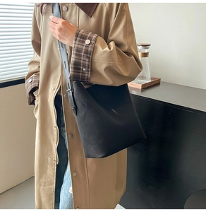 Detail of minimalist black suede bucket bag with leather strap on a trench coat model