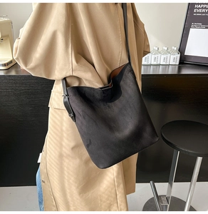 Close-up of black suede bucket bag styled with a beige trench coat in a cozy cafe