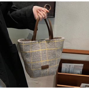 Detail of plaid wool tote bag featuring brown leather handles and a textured vintage design