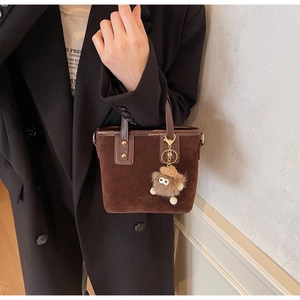 Détail du sac à main en daim marron foncé avec poignées et breloque peluche monstre