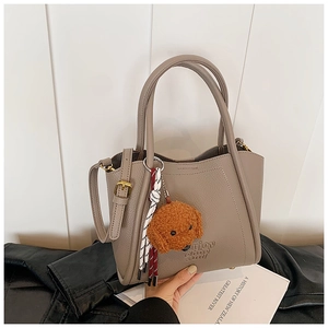 Détail du sac seau en cuir grainé taupe avec charm de chien en peluche et pompon