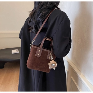 Sac fourre-tout en daim marron avec breloque en peluche et bandoulière porté par un mannequin
