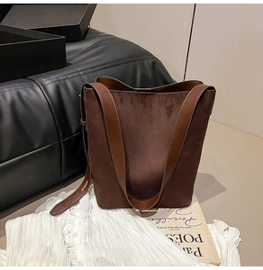 Close-up of dark brown suede bucket bag texture with leather strap on a sofa