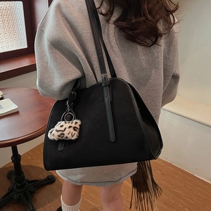 Détail du sac fourre-tout noir en daim avec pompon léopard sur l'épaule du modèle