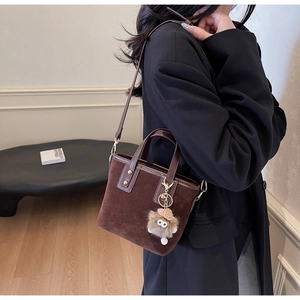 Détail du sac seau en daim marron foncé avec bandoulière en cuir et breloque pompon