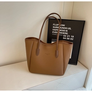 Detail of a brown lychee pattern leather tote bag with shoulder strap on a textured surface