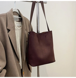 Detail of deep brown suede bucket bag with wide shoulder strap in office setting