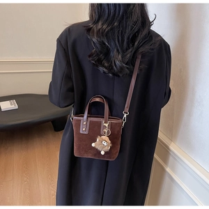 Détail d'un sac seau en daim marron avec bandoulière et breloque en peluche
