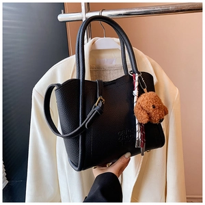 Détail d'un sac cabas noir avec grain de cuir, charm chien en peluche et cordon tressé