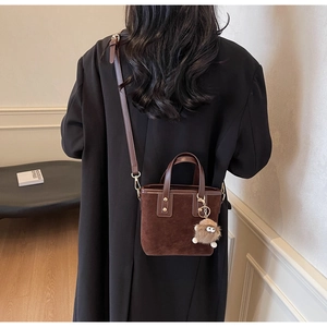 Gros plan sur le sac seau en daim marron avec breloque peluche porté à l'épaule