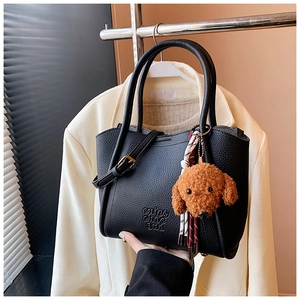 Détail du sac seau en cuir grainé noir avec charme ours en peluche et boucle dorée