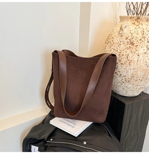 Detail of dark brown suede bucket bag with smooth leather strap in a minimalist setting