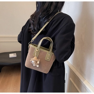 Détail d'un sac seau en daim marron avec des anses olive et un pendentif de mouton