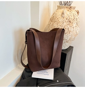 Detailed view of dark brown suede bucket bag with smooth leather strap in minimalist setting