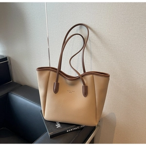 Close-up of beige lychee grain tote bag with dark brown straps on a black seat