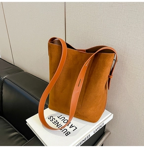 Detail of brown suede bucket bag featuring orange leather strap and adjustable metal buckle