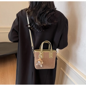 Détail d'un sac seau vintage en daim avec poignées en cuir olive et charme de monstre