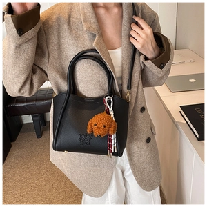 Détail du sac à main noir en cuir grainé avec breloque chien en peluche et bandoulière