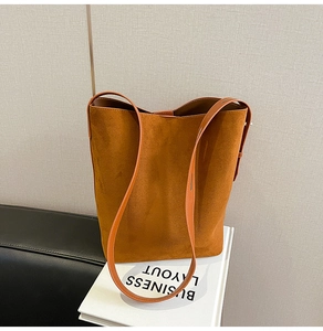 Detailed view of large brown suede bucket bag with leather strap on a decorative book