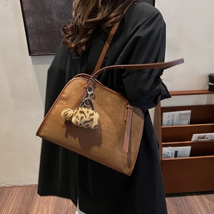 Sac fourre-tout marron en daim avec pompon léopard présenté dans un cadre chaleureux