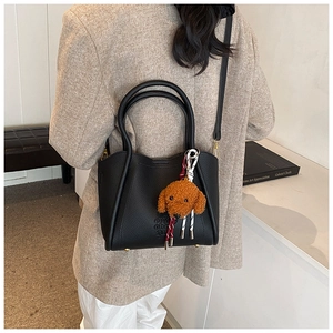 Détail du sac seau en cuir noir avec breloque chien en peluche et bandoulière
